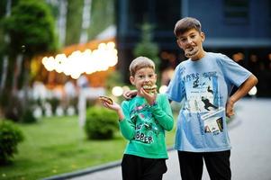 Two brothers with doughnuts at evening yard. Tasty yummy donut food. photo