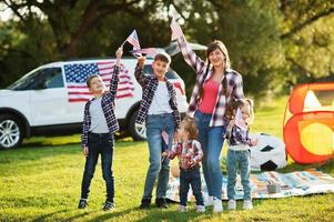 American family spending time together. With USA flags against big suv car outdoor. photo