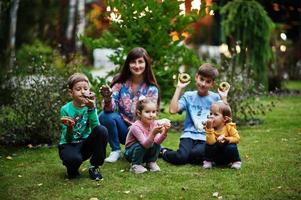 Four kids with mother eat doughnuts at evening yard. Tasty yummy donut food. photo