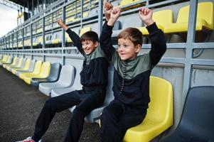 Two brothers support their favorite team, sitting on the sports podium at the stadium. photo