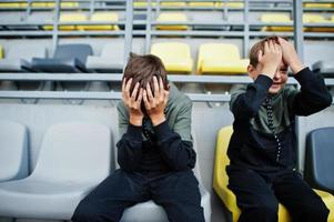 Oh no, they lost the game.Two brothers support their favorite team, sitting on the sports podium at the stadium. photo