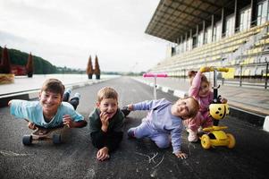 cuatro niños en asfalto juegan y se divierten. la familia deportiva pasa tiempo libre al aire libre con scooters y patines. foto