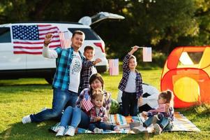 large american family spending time together. With USA flags against big suv car outdoor. America holiday. Four kids. photo