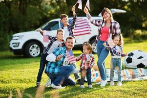 large american family spending time together. With USA flags against big suv car outdoor. America holiday. Four kids. photo