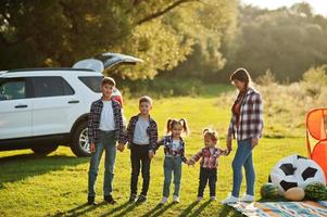 Family spending time together. Mother with four kids standing and holding hands against white suv car. photo