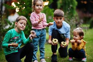 Four kids with doughnuts at evening yard. Tasty yummy donut food. photo