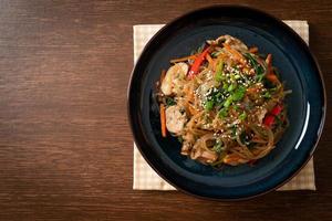 japchae or stir-fried Korean vermicelli noodles with vegetables and pork topped with white sesame photo