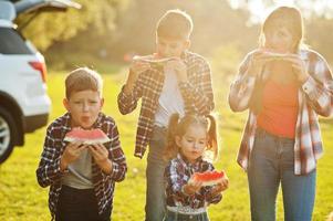 Family spending time together. Three kids with mother eat watermelon outdoor. photo