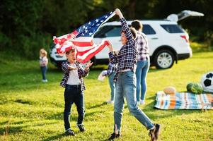 familia americana pasando tiempo juntos. los hermanos juegan con banderas de estados unidos contra un gran camión todoterreno al aire libre. América celebrando. foto