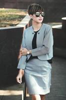 Fashion short hair business woman in sunglasses at the park. Stylish model in gray blazer and skirt photo