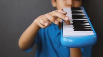 niño tocando instrumento musical de melodeón azul, órgano de soplado melódica, pianica o melodion en fondo gris oscuro foto