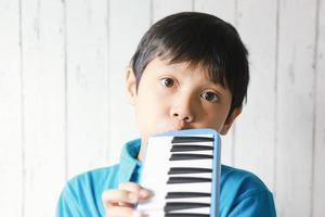 niño tocando instrumento musical de melodeón azul, órgano de soplado melódica, pianica o melodion sobre fondo blanco borroso. foto