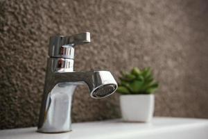 Metal tap on washbasin, with blurred succulent and cement wall background photo