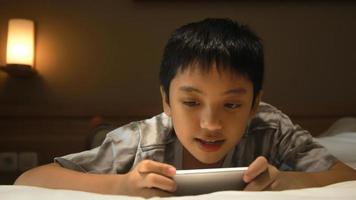 Asian boy lies in the white bed and plays with his smartphone photo