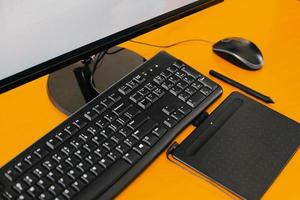 herramientas de oficina modernas negras, monitor de PC, teclado, mouse, tableta de lápiz de dibujo, lápiz óptico, en mesa amarilla foto