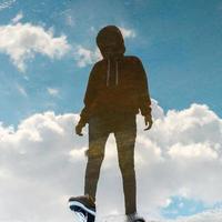 Reflection in water of man with wearing hoodie and ripped jeans standing in bright blue sky. Image contains grain and blurry because it came from water reflection photo