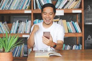 Man have a good news from cell phone when reading a book In Library. Happy expression photo