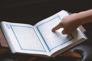 Hand of young muslim man reading the holy Quran. Muslim man studying The Quran at home. Waiting iftar in Ramadhan. photo