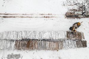 Loader loads logs stacked in piles covered with snow top view photo