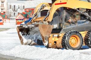 The compact and agile grader with hydraulic front blade clears snow from the city square. photo