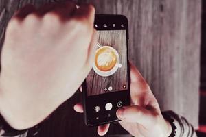 las manos sostienen un teléfono y una taza de café foto