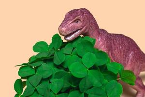 St. Patrick's Day happy dinosaur, a bouquet of clover in a bucket and gold coins on a beige background. Closeup copy space photo