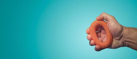 Banner with a man hand pressing at a red rubber wrist expender at turquoise gradient background with copy space. Concept of health, sport and active lifestyle. photo