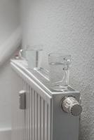 House heating battery with maximum heating power setting and glasses of water standing on it to decrease air dryness at smooth background with copy space. Concept of comfort of home living lifehacks. photo
