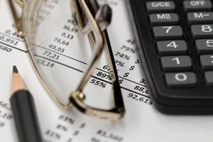 Financial report, glasses, calculator and pencil on the table in the office. A paper sheet full of business data. Accounts number on the data paper. Business documents on office table. Closeup. photo