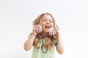 Cheerful little girl in headphones on white background. Music or entertainment online. Happy kid photo