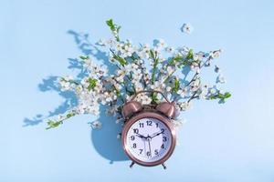 Alarm clock and blossom branches on a blue background. Flat lay, top view composition photo