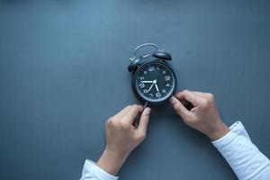 person hand holding alarm clock black background , photo