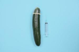 educación sexual con pepino anticonceptivo y jeringa aislado sobre fondo azul foto