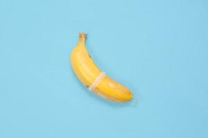 educación sexual con plátano y condón aislado sobre fondo azul foto