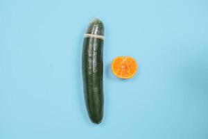 educación sexual con anticoncepción pepino y naranja aislado sobre fondo azul foto