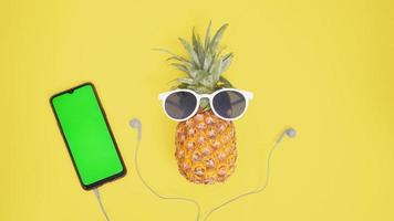 pineapple fruit in glasses and smartphone and headset isolated on yellow background photo