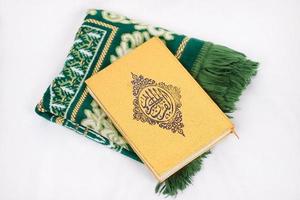 el libro sagrado al quran y la alfombra de oración aislado sobre fondo blanco foto