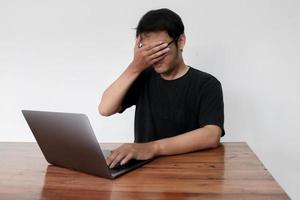 Young asian man hiding his face with hand because shocked and embarrassed by some porn videos or another forbidden thing he saw on the internet using a laptop photo