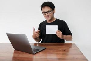 Young Asian man feeling happy with laptop and holding empty white space paper. Smile Indonesia Man wear black shirt Isolated grey background. photo