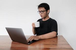 Young Asian Man is confused and shocked when calling in the phone with the laptop beside it. Indonesian man wearing a blue shirt photo
