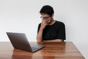 Young Asian man is serious work or thinking in the front the laptop. Indonesia Man wear black shirt Isolated grey background. photo