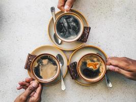 Three People hands holding cups of black coffee and chocolate cookies isolated on white table photo