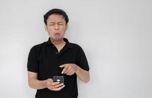 un joven asiático llora y se entristece cuando mira el teléfono inteligente. indonesia hombre usar camisa negra aislado fondo gris foto