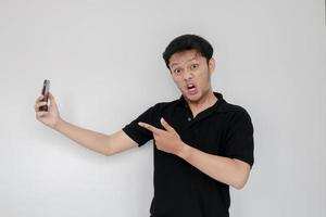 Angry Asian young man get mad on the smartphone. Indonesia Man wear black shirt Isolated grey background photo