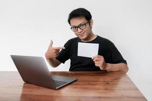 Young Asian man feeling happy with laptop and holding empty white space paper. Smile Indonesia Man wear black shirt Isolated grey background. photo