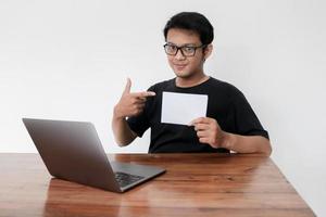 Young Asian man feeling happy with laptop and holding empty white space paper. Smile Indonesia Man wear black shirt Isolated grey background. photo