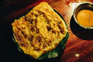 Roti Canai or Canai Bread or Parata Bread or prata Bread with curry sauce on the banana leaf plate isolated on wooden background with dark background and spotlight photo