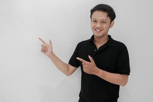 Happy and smile of young Asian man with hand point on empty space. Indonesia Man wear black shirt Isolated grey background photo