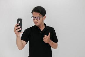 Wow face of Your Asian man shocked what he see in the smartphone on isolated grey background. Indonesia Man wear black shirt Isolated grey background photo