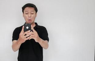 Young Asian man cry and sad when looking on the smartphone. Indonesia Man wear black shirt Isolated grey background photo